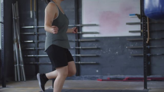 Tilt down slow motion shot of professional female athlete performing jump rope alternate foot step jumps while exercising in gym