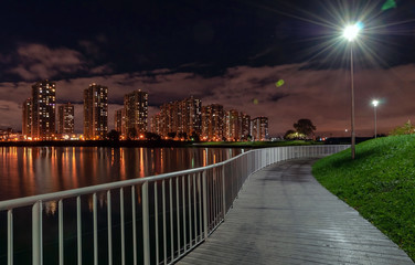 Fototapeta na wymiar Night city landscape - high-rise houses with lighted windows on the shore of the pond, dark sky with clouds and reflection in the water