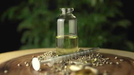 Focus shift. Medical cannabis hemp seeds various medications. Pills, THC capsules, cbd oil, syringe and glass jar bottle with concentrate on the wooden table near green marijuana plant macro closeup.