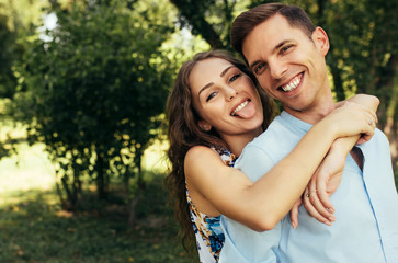 Close-up outdoor portrait of romantic couple in love dating outdoors at the park on a sunny day. Happy couple embracing each other and making grimmace. Date day. Valentine day