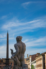Fototapeta na wymiar A concrete statue of an ancient roman male god back view at Piazza Navona looking at the airplane in the blue sky
