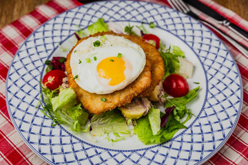 Schnitzel with vegetables and fried egg. Fork and knife, checkered red and white napkin. Horizontal close-up