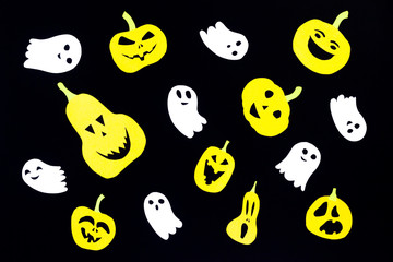 A colored background made of groups of pumpkins cut out of orange paper and of ghosts made of white paper isolated on a black background is ideal for the holiday of all saints - Halloween.