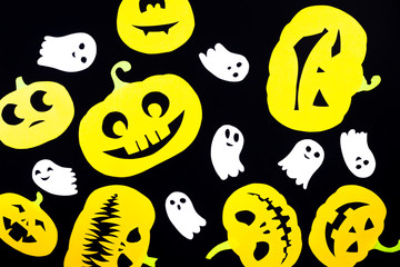 A colored background made of groups of pumpkins cut out of orange paper and of ghosts made of white paper isolated on a black background is ideal for the holiday of all saints - Halloween.