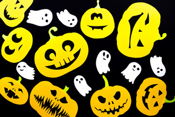 Obraz premium A colored background made of groups of pumpkins cut out of orange paper and of ghosts made of white paper isolated on a black background is ideal for the holiday of all saints - Halloween.