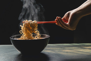 Steam and smoke Instant noodles in bowl on wooden table and nature light and black background,...