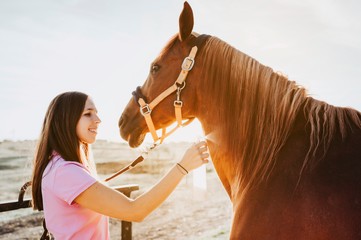 Side view of woman spraying skin of sorrel horse with special liquid while standing in light barn