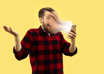 Young man using smartphone isolated on yellow studio background. Concept of human emotions, facial...
