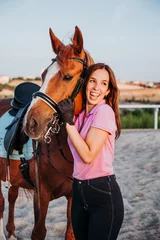Foto op Canvas Young smiling woman standing in relax outside with wonderful chestnut horse on bridle and looking away. © karrastock