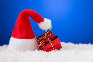 Santa Claus hat on snow with gift box and blue background with copy space
