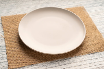 Beige round plate on a sackcloth on a wooden white table