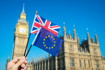 Fototapeta na wymiar Hand waving European Union and British Union Jack flag in front of Big Ben and the Houses of Parliament at Westminster Palace, London, UK as the Brexit process moves ahead