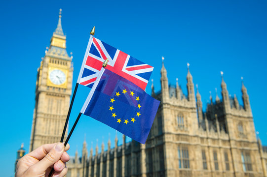 Hand waving European Union and British Union Jack flag in front of Big Ben and the Houses of Parliament at Westminster Palace, London, UK as the Brexit process moves ahead