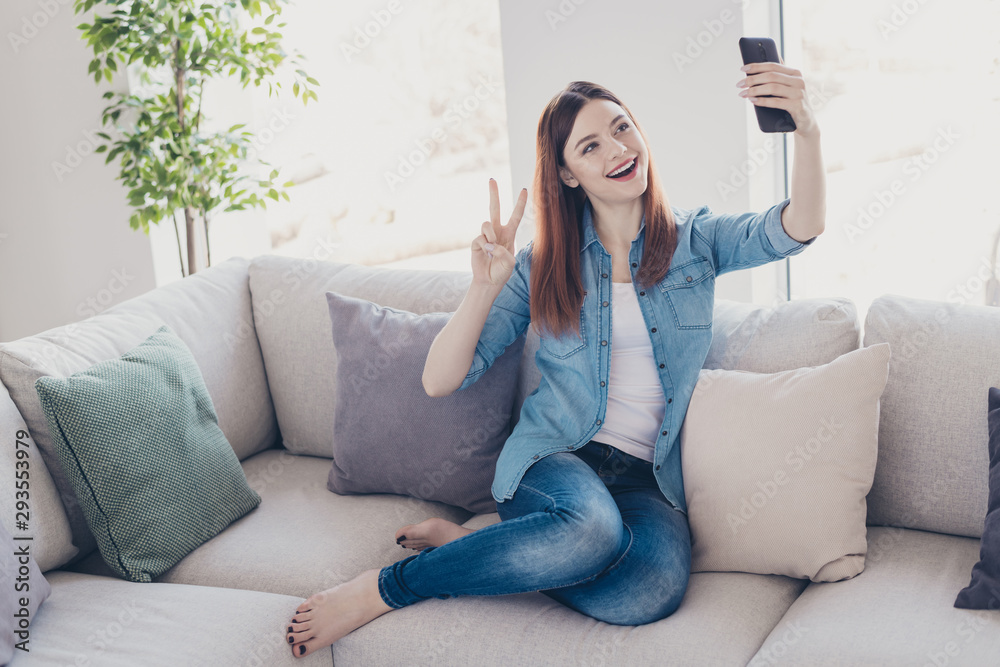 Sticker Photo of pretty lady with telephone in hands making selfies showing v-sign symbol sitting comfy on sofa wearing jeans clothes apartment indoors