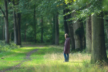 Obraz premium Woman in coat on sunny forest path in early fall.