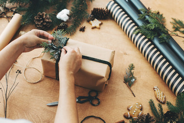 Hands wrapping rustic christmas gift, tying green twine ,and pine branches, cones, gingerbread...