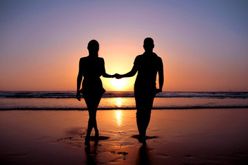 Fototapeta na wymiar Silhouette of a young couple in love who holds hands on the beach at sunset