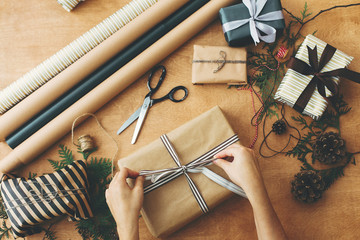 Merry Christmas, flat lay. Hands wrapping stylish christmas gift box in craft paper and scissors,...