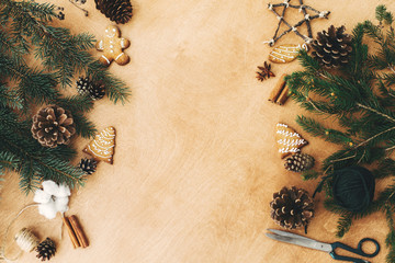 Christmas rustic flat lay. Stylish christmas frame of pine branches, cones, gingerbread cookies,thread, cinnamon, anise on rural wooden table. Space text. Seasons greeting card mockup