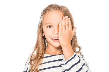 front view of smiling kid covering eye with hand isolated on white