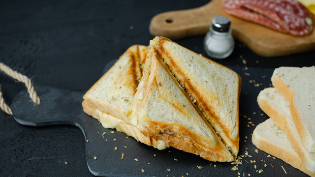 Tosty z serem i salami leżące na kamiennej desce. Ciemne tło, zbliżenie.