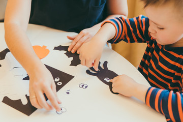 young mother with toddler son making craft spiders for halloween holiday