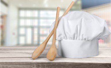 White cooks cap and wooden spoons on wooden table