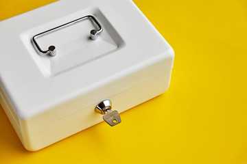 Close up of small white closed cashbox or money box with key in lock on yellow background with copy space  