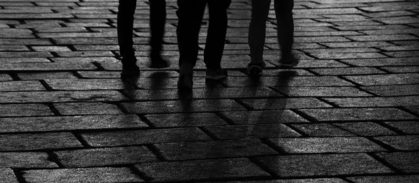 Dark silhouettes of three people walking in the evening on street. Shadows and light reflection. Urban nightlife modern ballet scene. Abstract mystery background. Black white banner photo.