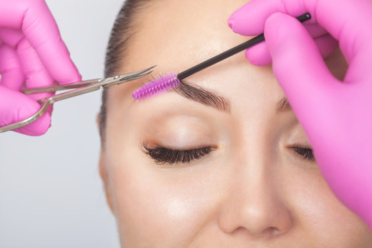 The make-up artist cuts eyebrows with scissors. A girl with beautiful long eyelashes and well-groomed eyebrows.