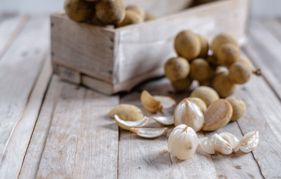 Mix of peeled and clusters whole of exotic Thai fruit called Longkong or lansium parasiticumor southern langsat on wooden table and background. It is a famous sweet tropical fruit in southeast asia.
