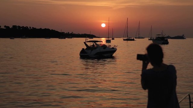 Sillhouette of a woman shooting photos of a yacht in a golden sunset over the sea