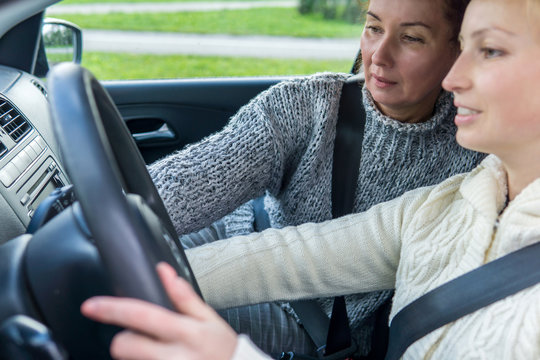 female driving instructor teaches a female student to drive a car