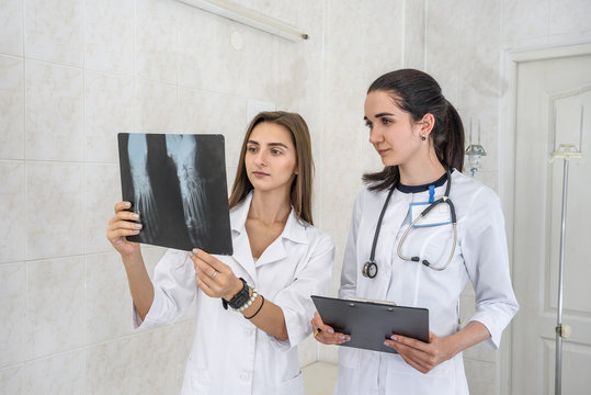 Doctor with young intern analyzing patient's x-ray in hospital. One woman holding and and they both looking on it