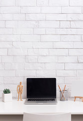 Fototapeta na wymiar Laptop with blank screen in front of bricks wall in stylish office
