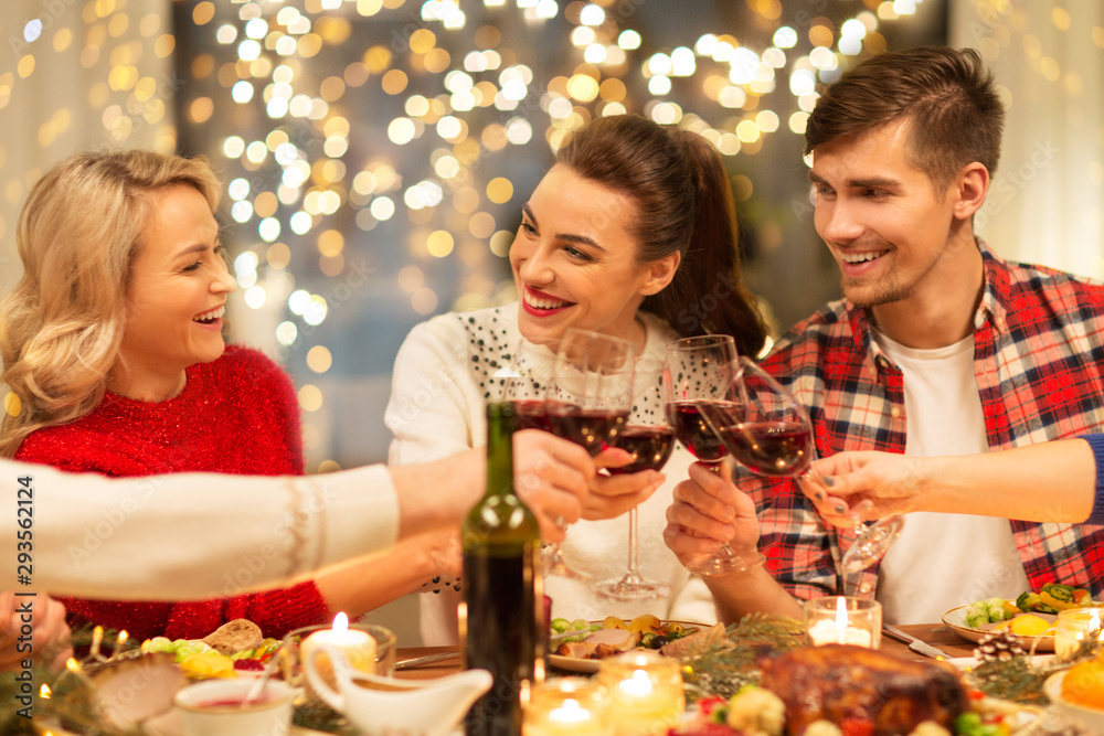 Wall mural holidays and celebration concept - happy friends having christmas dinner at home, drinking red wine 