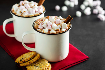 Two cups of hot chocolate, cocoa or warm drink with marshmallows and sweet cookies on dark background