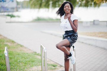 Obraz premium African american dark skinned slim model posed in a black leather shorts and white t-shirt.