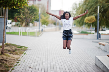 African american dark skinned slim model posed in a black leather shorts and white t-shirt. She jumping at the air.