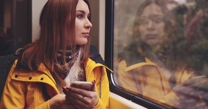 Young Woman Using Smartphone on a Train. SLOW MOTION 4K. Girl Looking Out of a Train Window during her daily commute, using cell phone. Social network, planning, communicating.