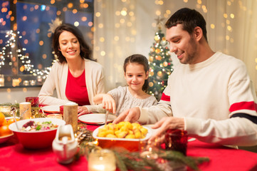 holidays, family and celebration concept - happy mother, father and little daughter having christmas dinner at home