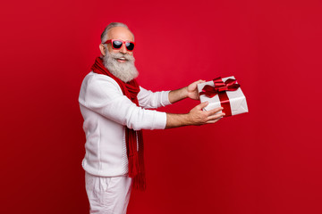 Aged fashion man giving big giftbox to grandchild wear sun specs knitted jumper isolated red...