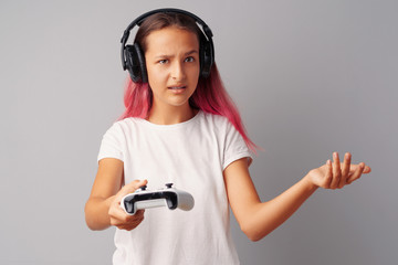 Young pretty teen girl playing with console joystick over a gray background