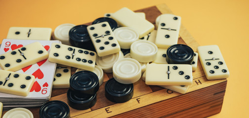 Various board games chess board, playing cards, dominoes on a orange background.