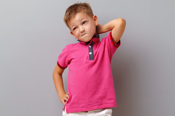 Portrait of thinking little boy standing on a grey background