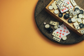 Various board games chess board, playing cards, dominoes on a old wooden table orange background.