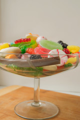 Delicious marmalade sweets of different shapes lie in a glass vase standing on a wooden board