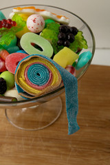 Multi-colored marmalade sweets of various shapes lie in a glass vase, standing on a wooden board coarsely twisted sweetness