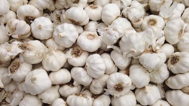 Slow motion zoom in tracking shot over a pile of white garlic bulbs, allium, sativum, on display on a market stall