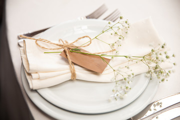 Wedding table setting for  banquet in restauran. Setting with white flowers and blank guest card. Cutlery, crockery.